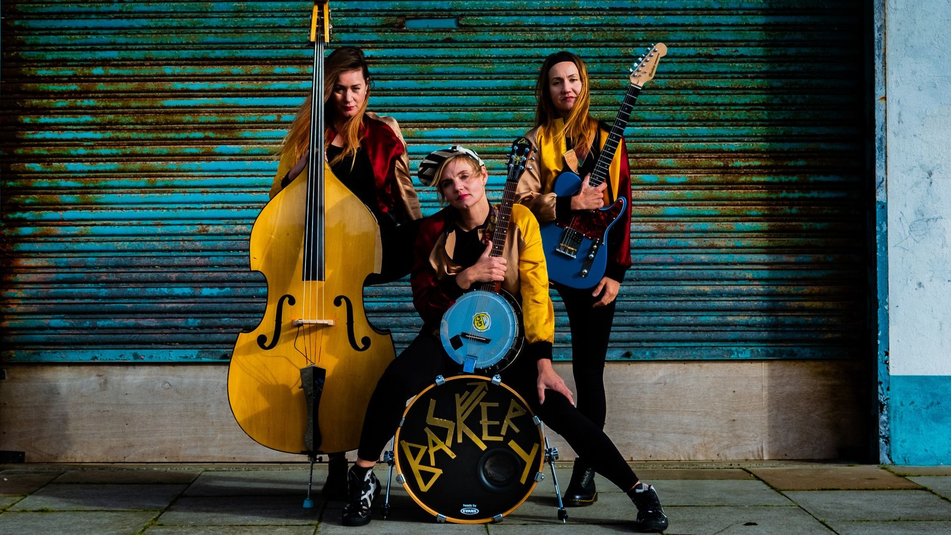 Den svenske trio Baskery med kontrabas, banjo og guitar foran rå baggrund.
