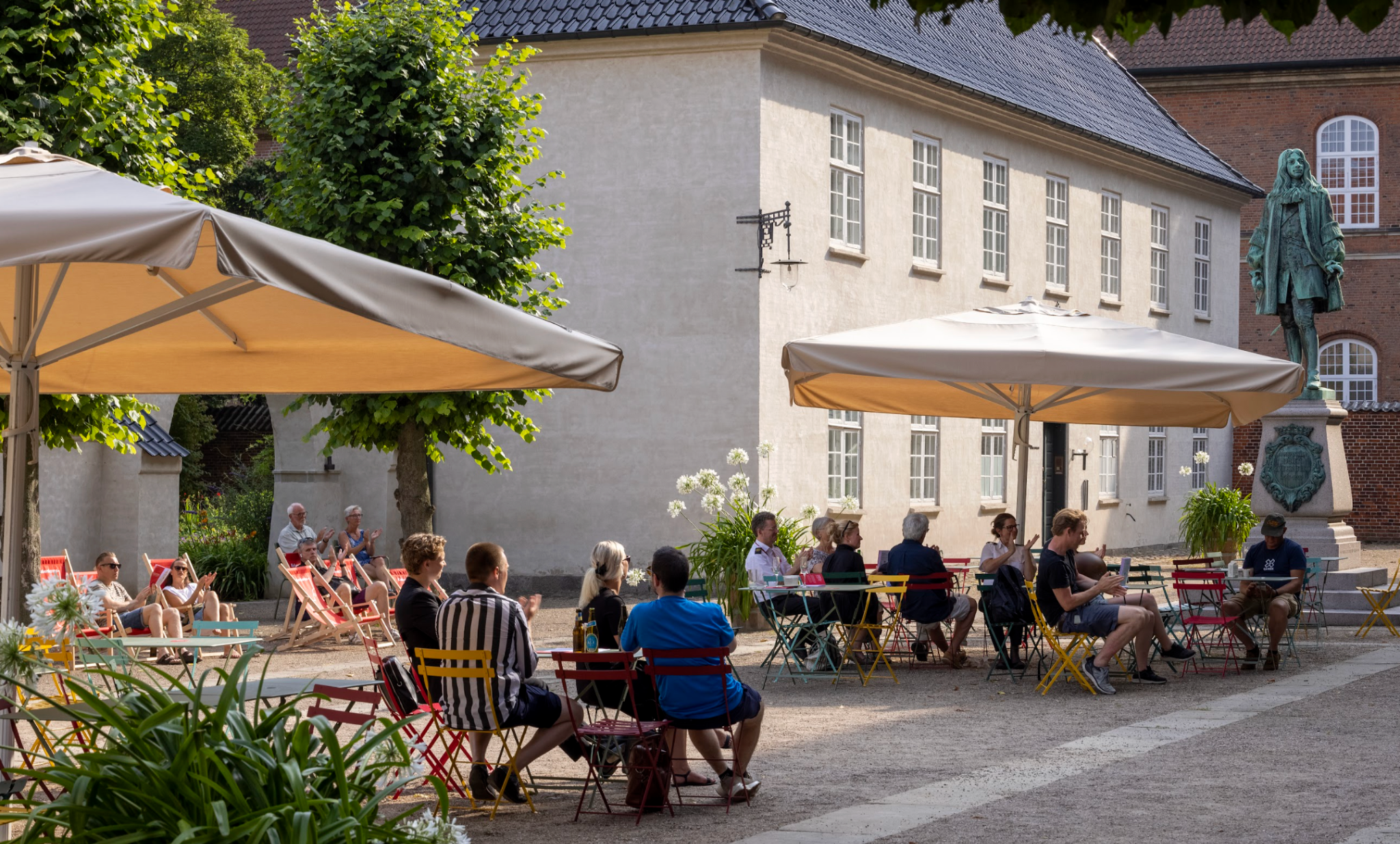Mennesker der sidder ved borde under parasoller i bibliotekshaven