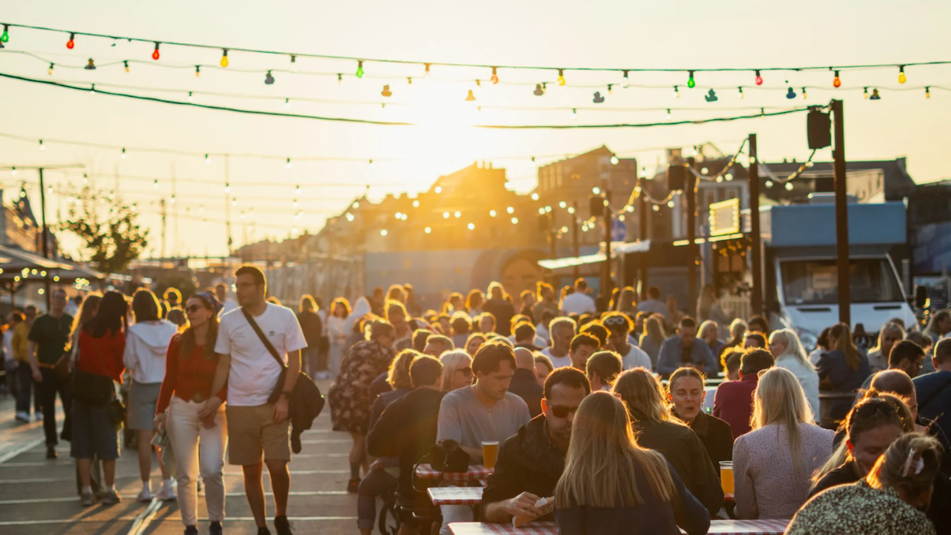 Stemningsbillede fra Broens Gadekøkken med høj sol og folk der sidder ved borde og drikker øl og spiser mad