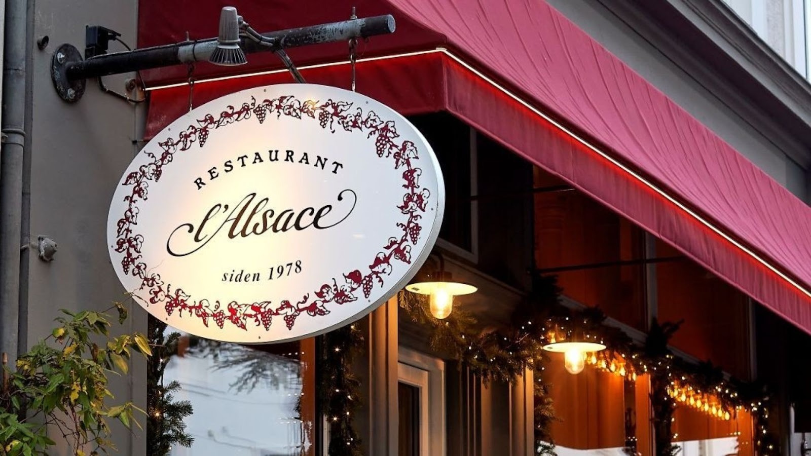 Fronten af resteaurant L'Alsace med skiltet hængende foran borde og lamper