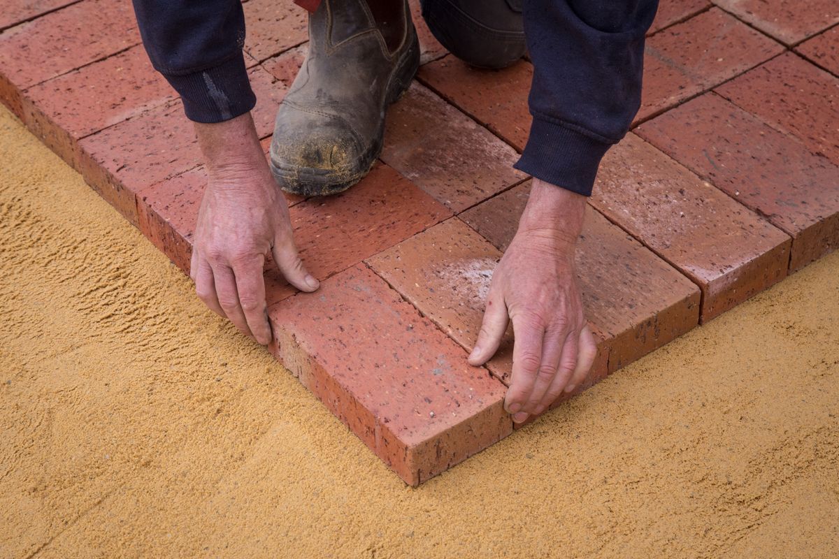 Worker setting pavers on a sand base