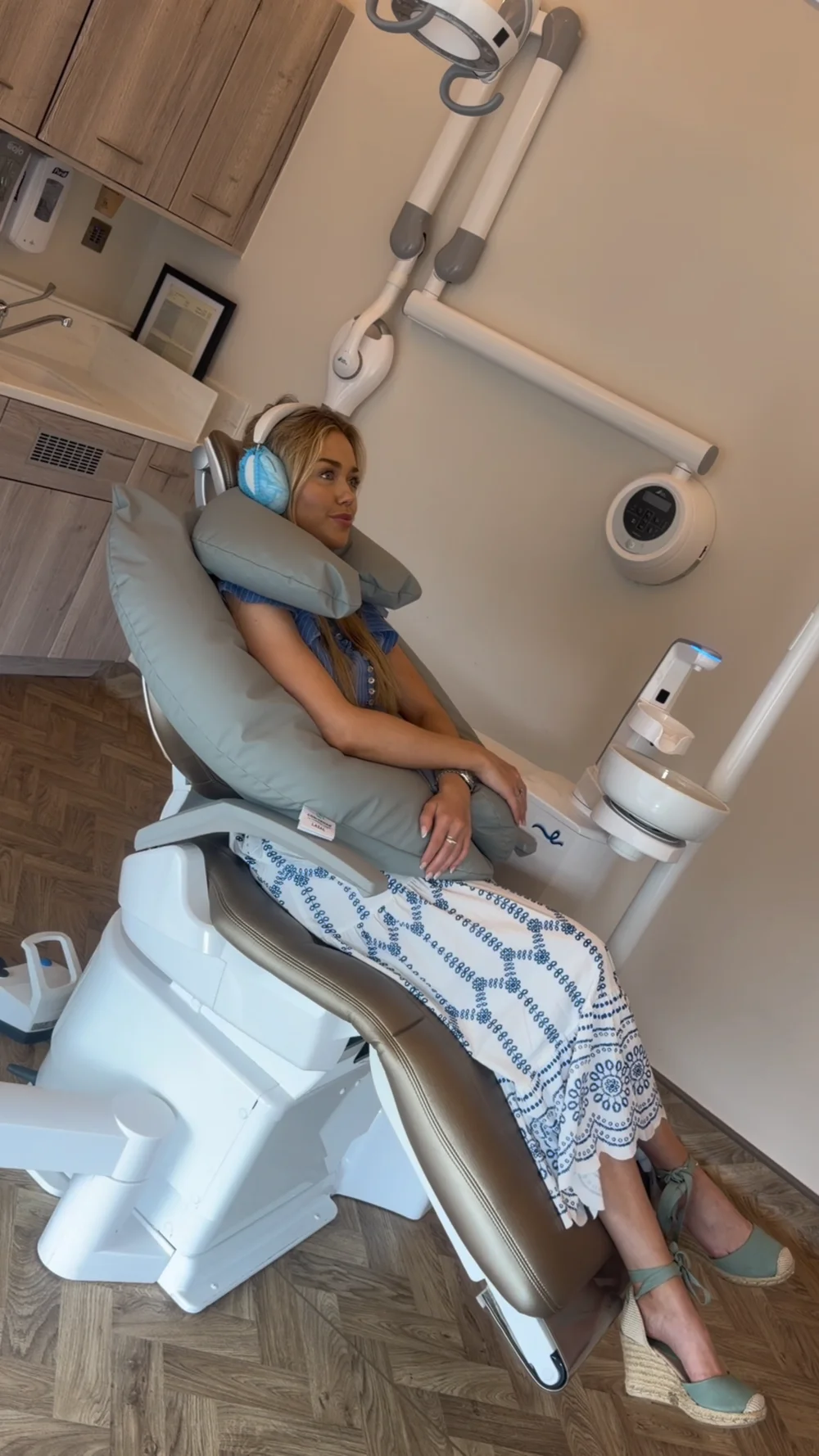 Wide view of the dental chair with a patient using grey positioning cushions and covered headphones.