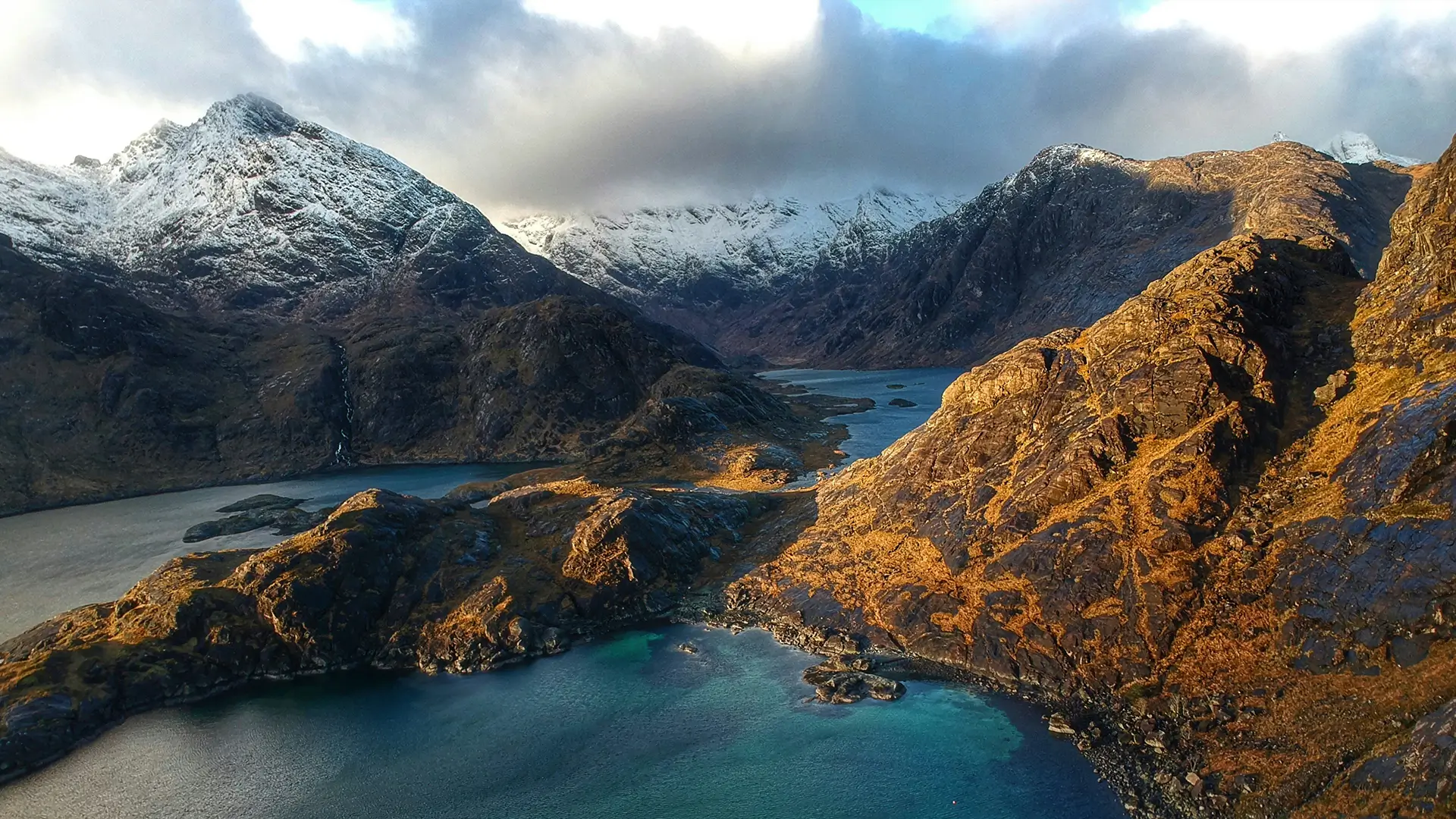 Sunset over a rugged path through shrubs with distant mountains under a partly cloudy sky.