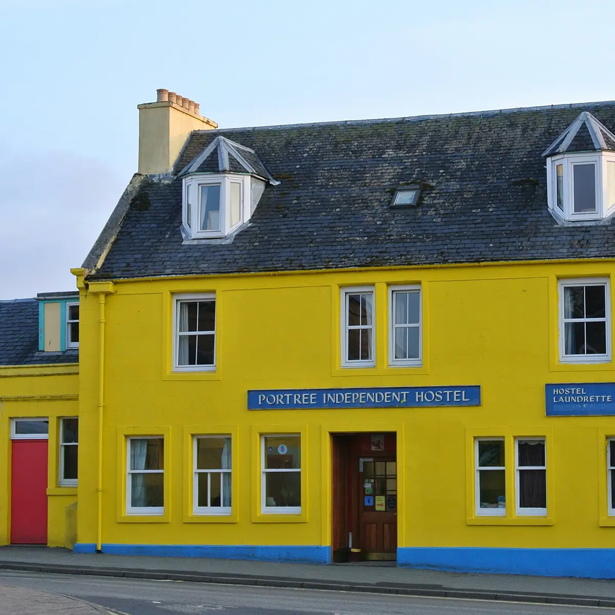 Bright yellow building labeled Portree Independent Hostel with blue trim and a red side door.