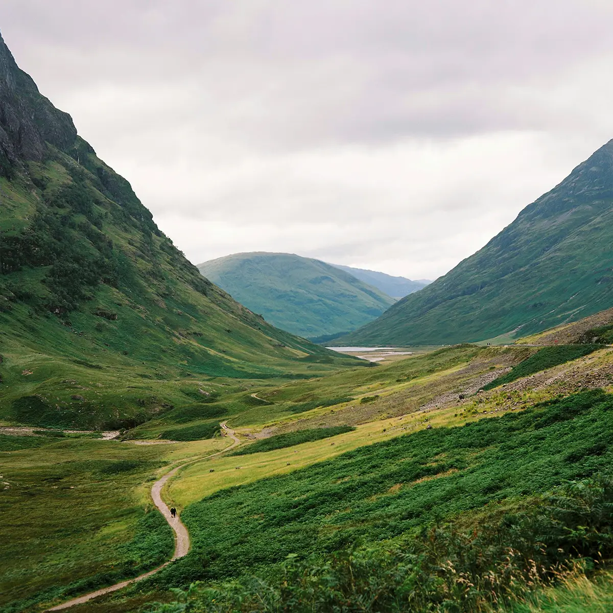 Green valley with winding path between steep hills under a cloudy sky.