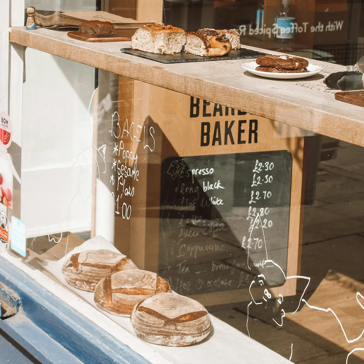 Bakery window showing assorted breads and pastries with handwritten menu reflecting inside.