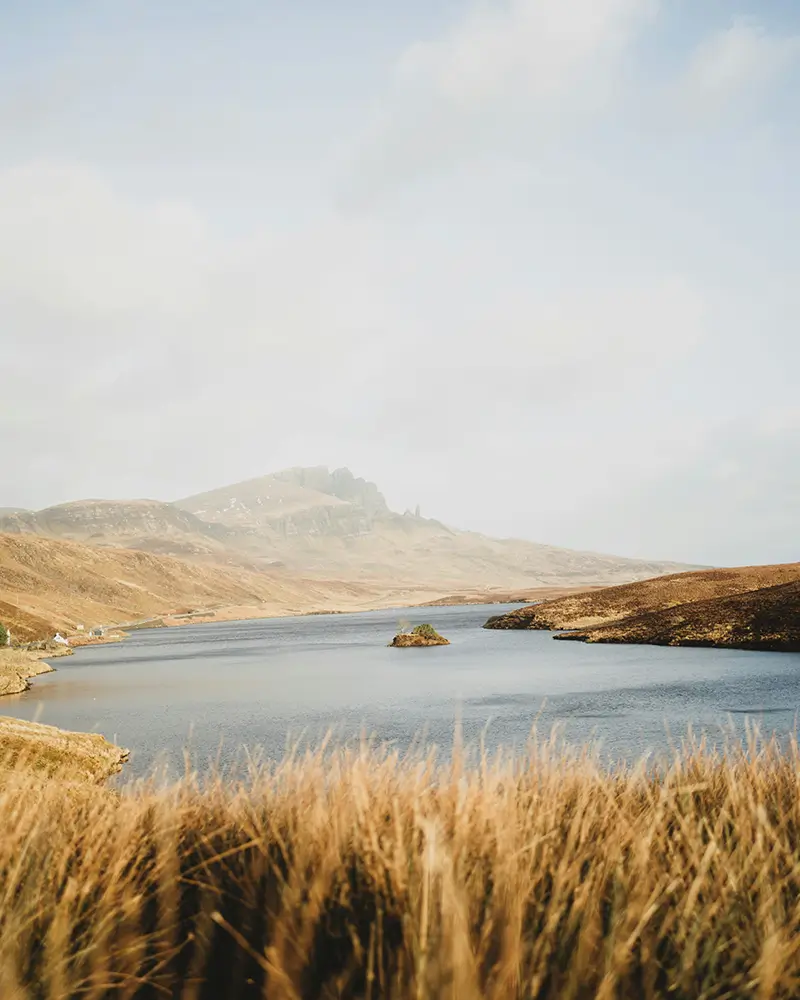 Tranquil lake surrounded by golden-brown grass and rolling hills under a cloudy sky.
