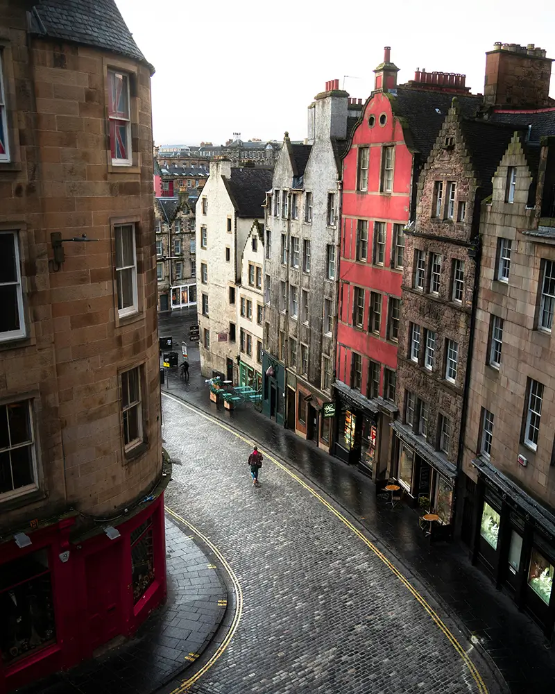 Curved cobblestone street lined with historic multi-story buildings in a wet, overcast setting.