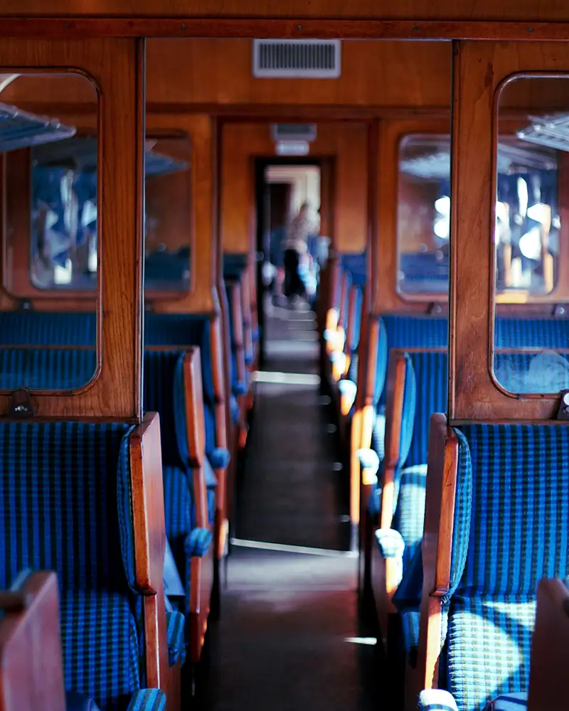 Interior aisle view of a vintage train car with wood paneling and blue checkered seats.