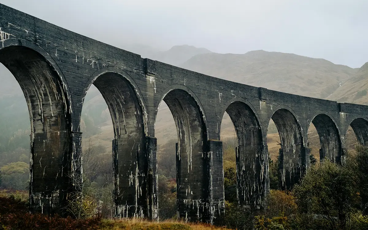 Viaduct bridge spanning autumn trees and hills in a golden-lit rural landscape.