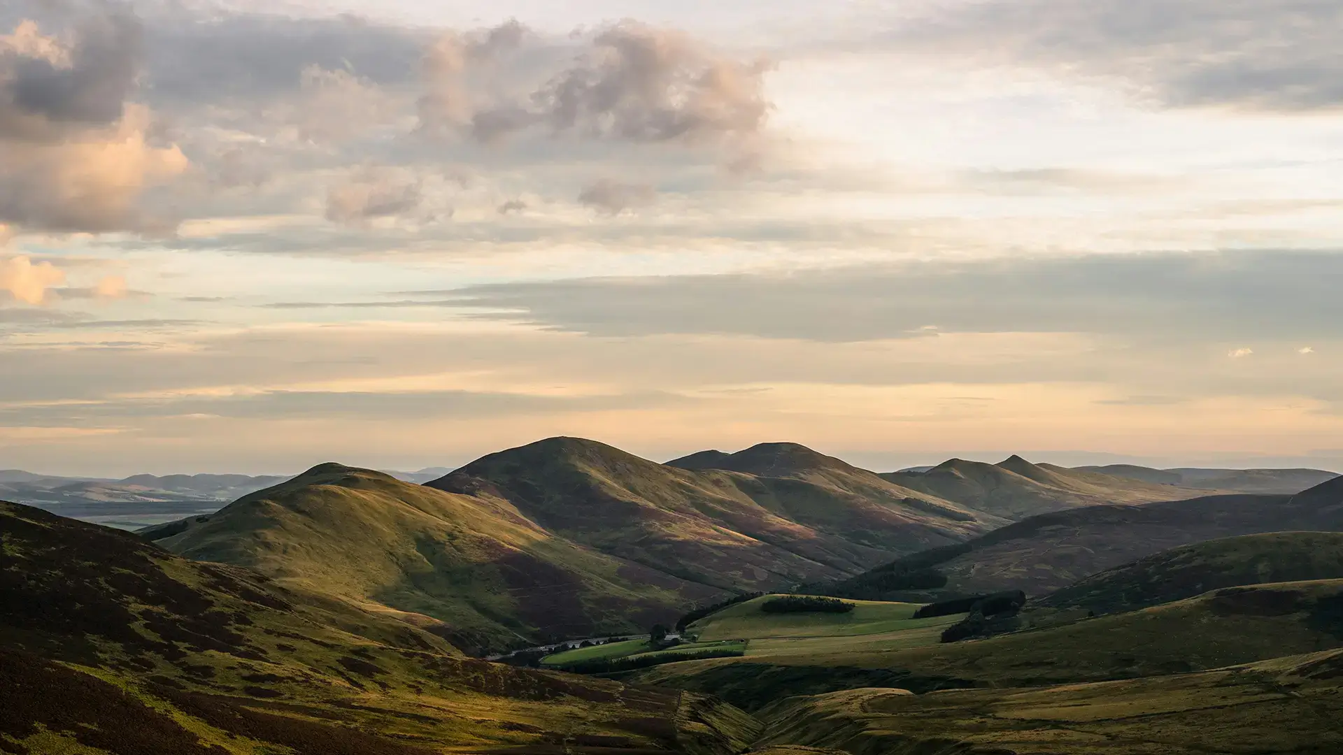 Sunlit rolling green hills under a cloudy sky during a calm late afternoon.