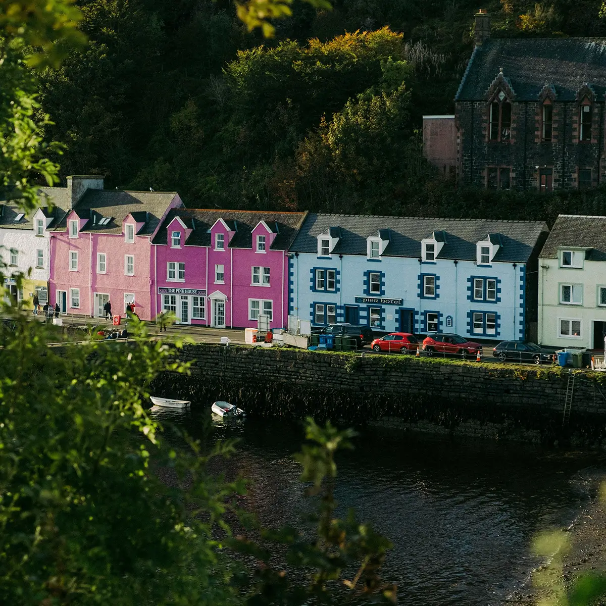 Colorful buildings including The Pink House and Pier Hotel by a waterfront with boats and trees.