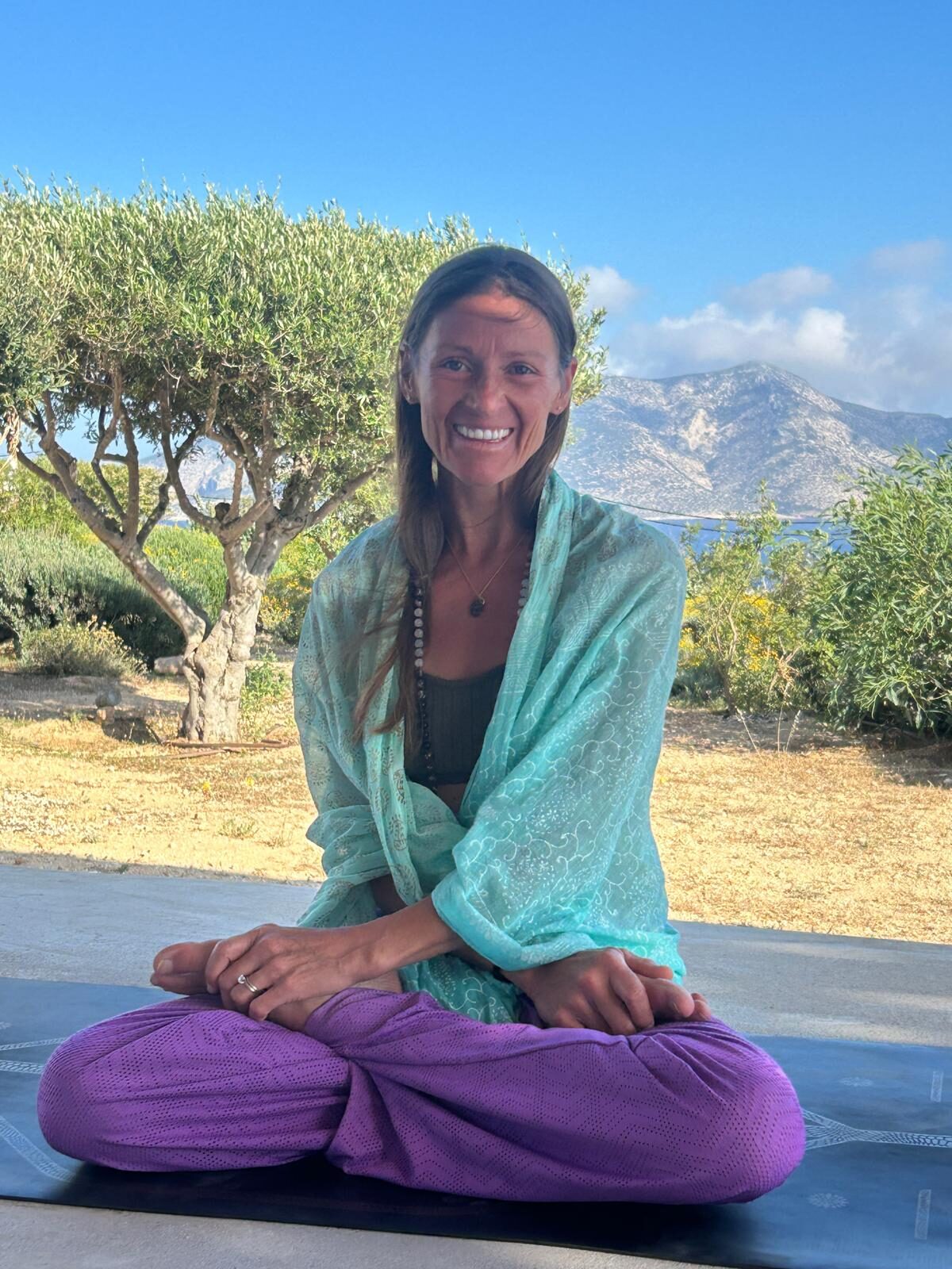 Rachel seated cross-legged in the shade of an olive tree