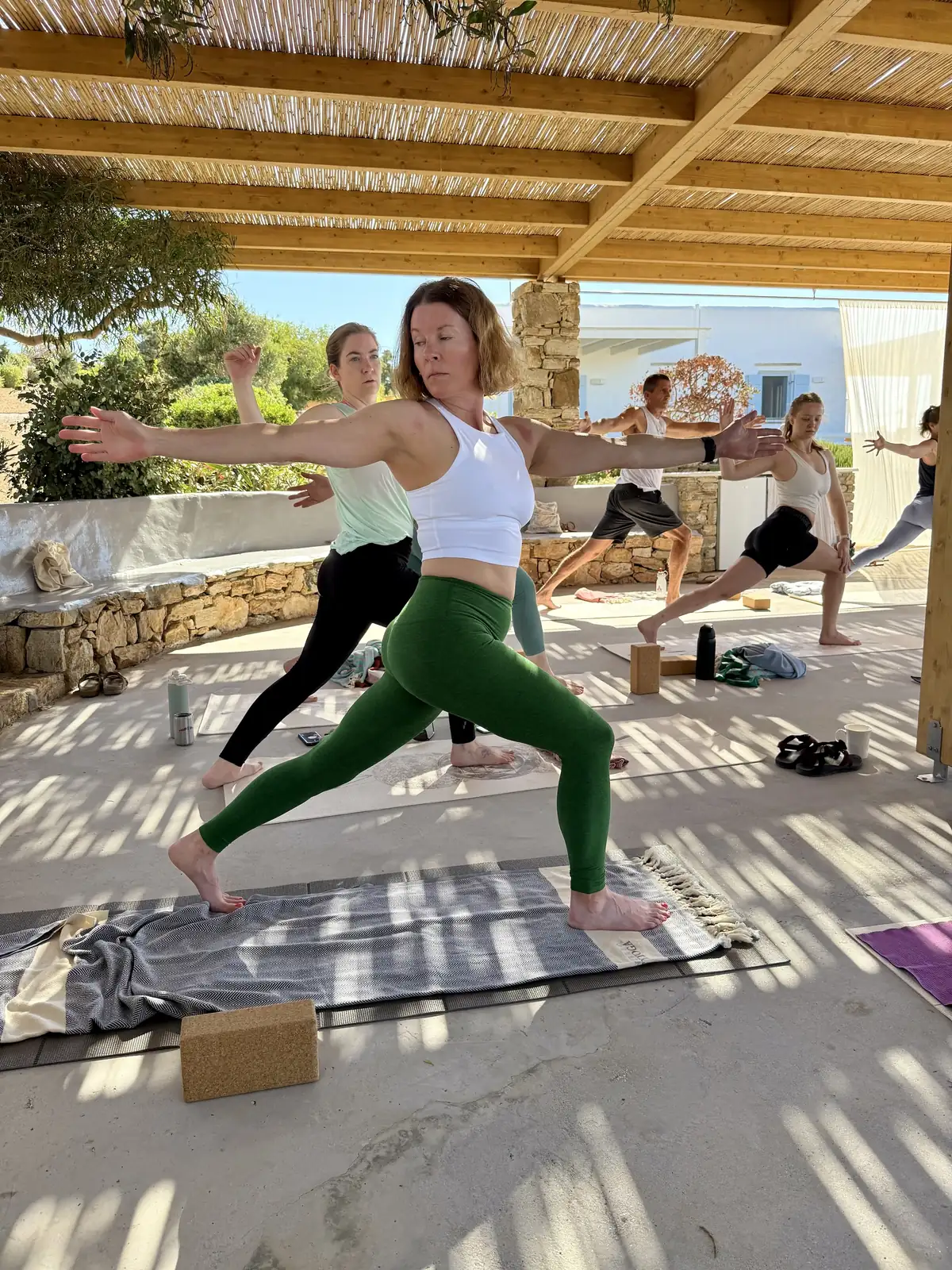 Rachel teaching warrior pose in the shade of the pergola