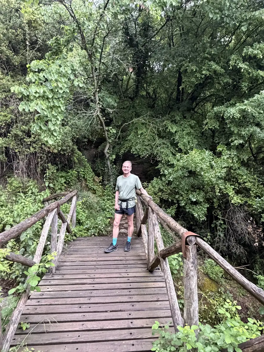 Two guests crossing a wooden footbridge on a forest trail in Meteora