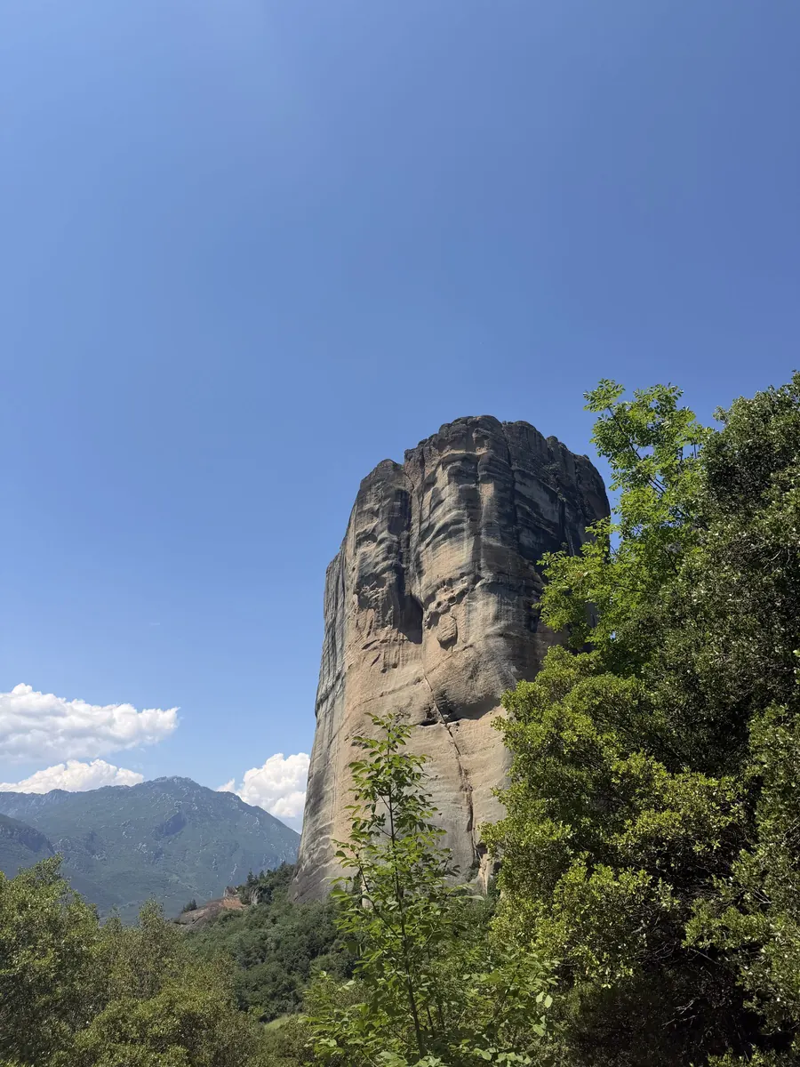 Massive sandstone rock pillar rising above the forest in Meteora