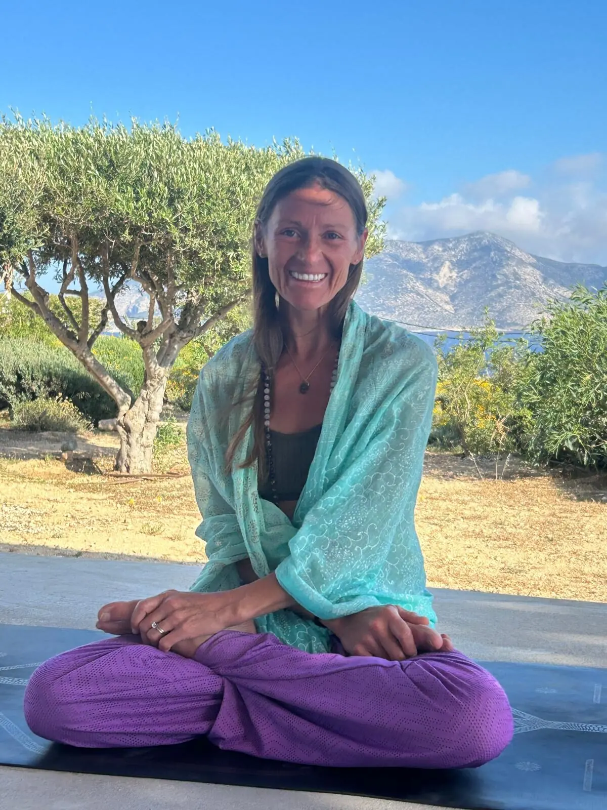 Rachel seated cross-legged in the shade of an olive tree