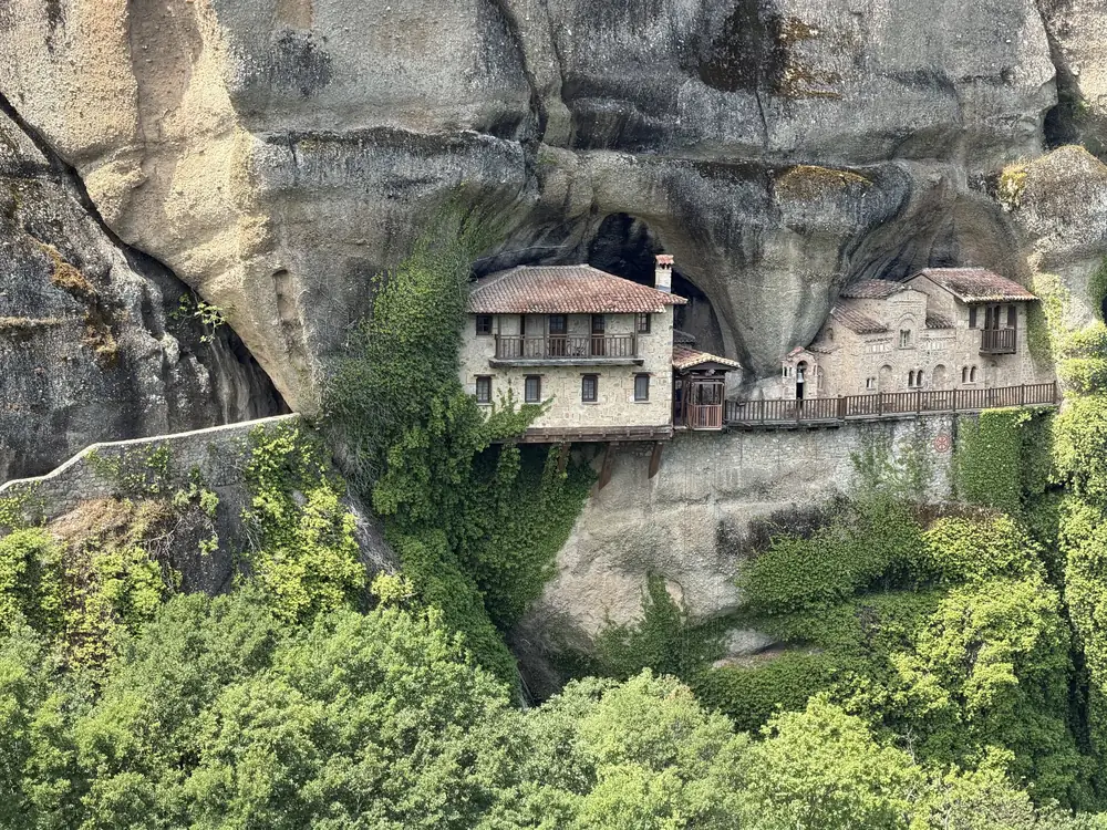 A red-roofed monastery built into the cave face of a rock pillar