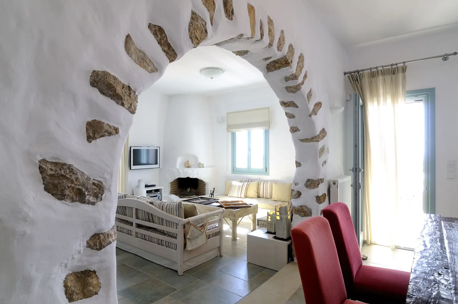 A whitewashed living room with a stone archway and fireplace