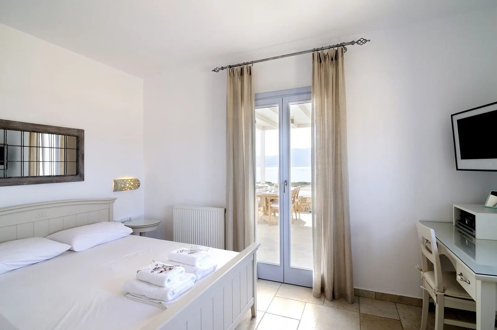 A bright white bedroom with doors opening onto a terrace
