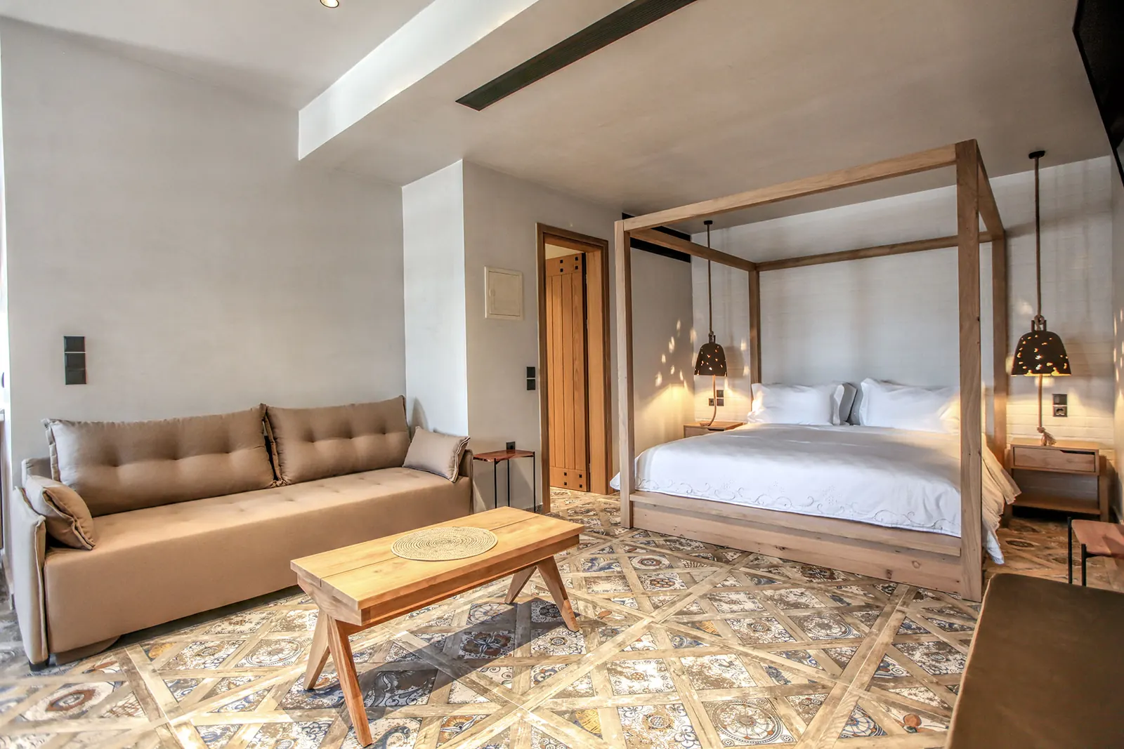 A suite with a four-poster bed, a sofa and a patterned tile floor