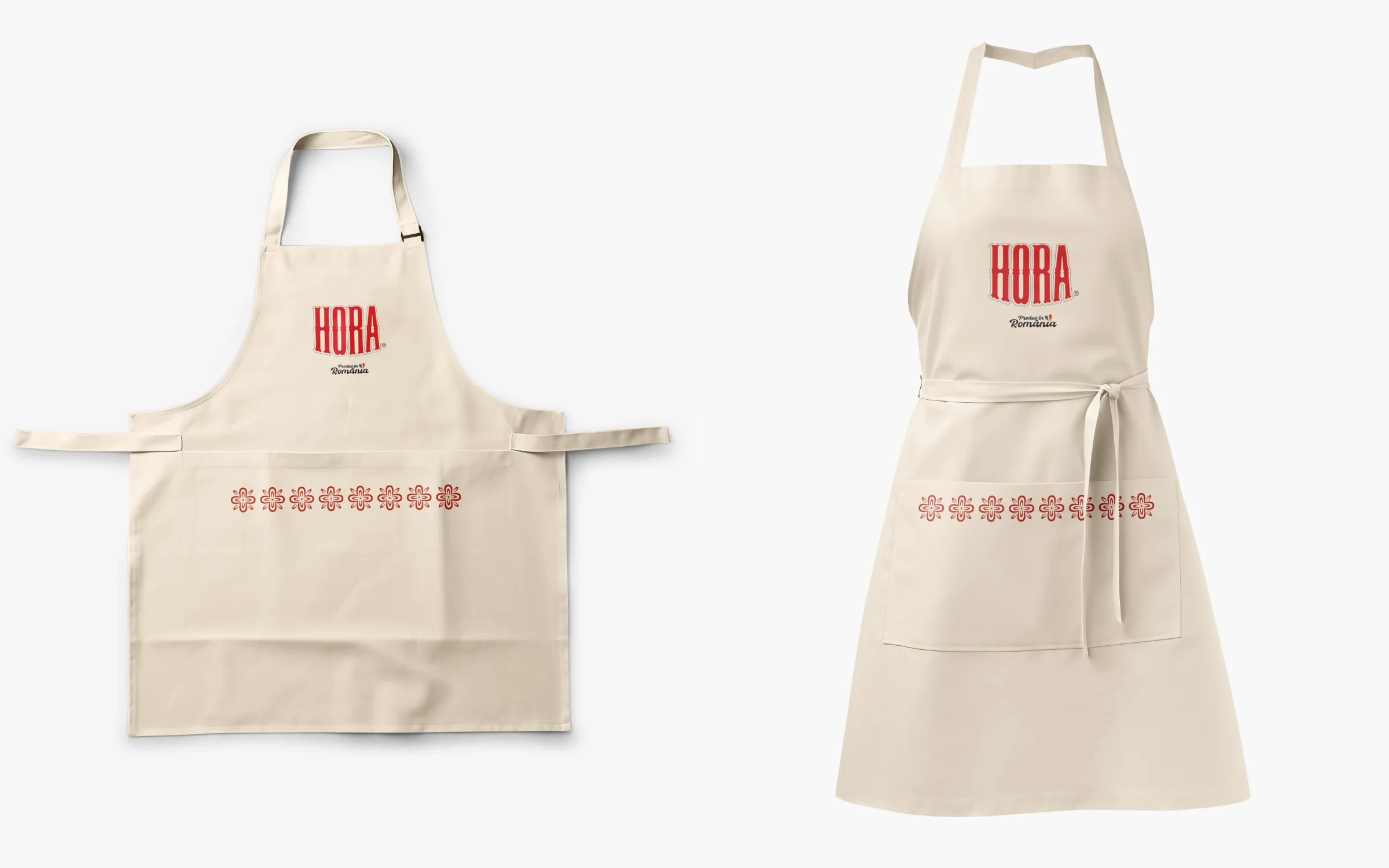 Two cream kitchen aprons with the red HORA wordmark and a band of red folk-embroidery motifs across the pocket.
