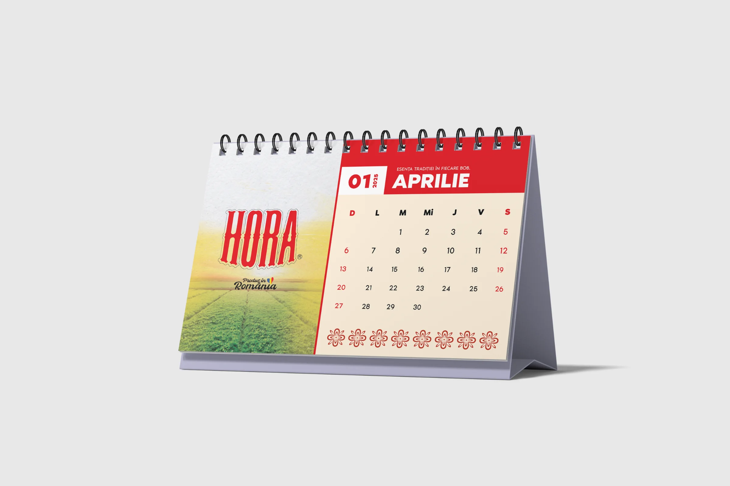 HORA desk calendar open on April: a red header with the HORA wordmark, the month grid and a red folk-embroidery border.