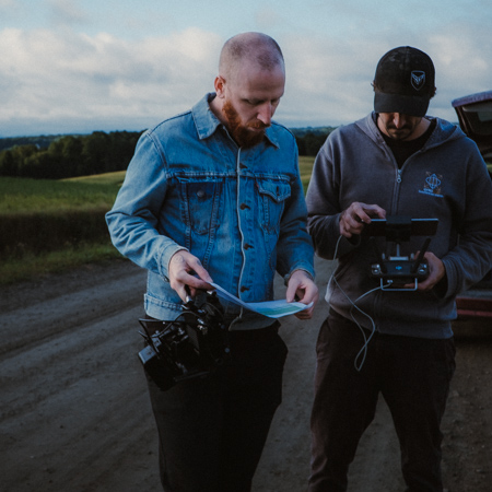 Deux hommes en plein air consultent un plan et un écran de contrôle d'appareil photo.