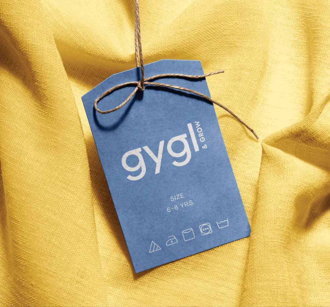 Blue clothing tag labeled 'gygl & GROW' on yellow fabric, indicating size 6-8 years with care symbols.