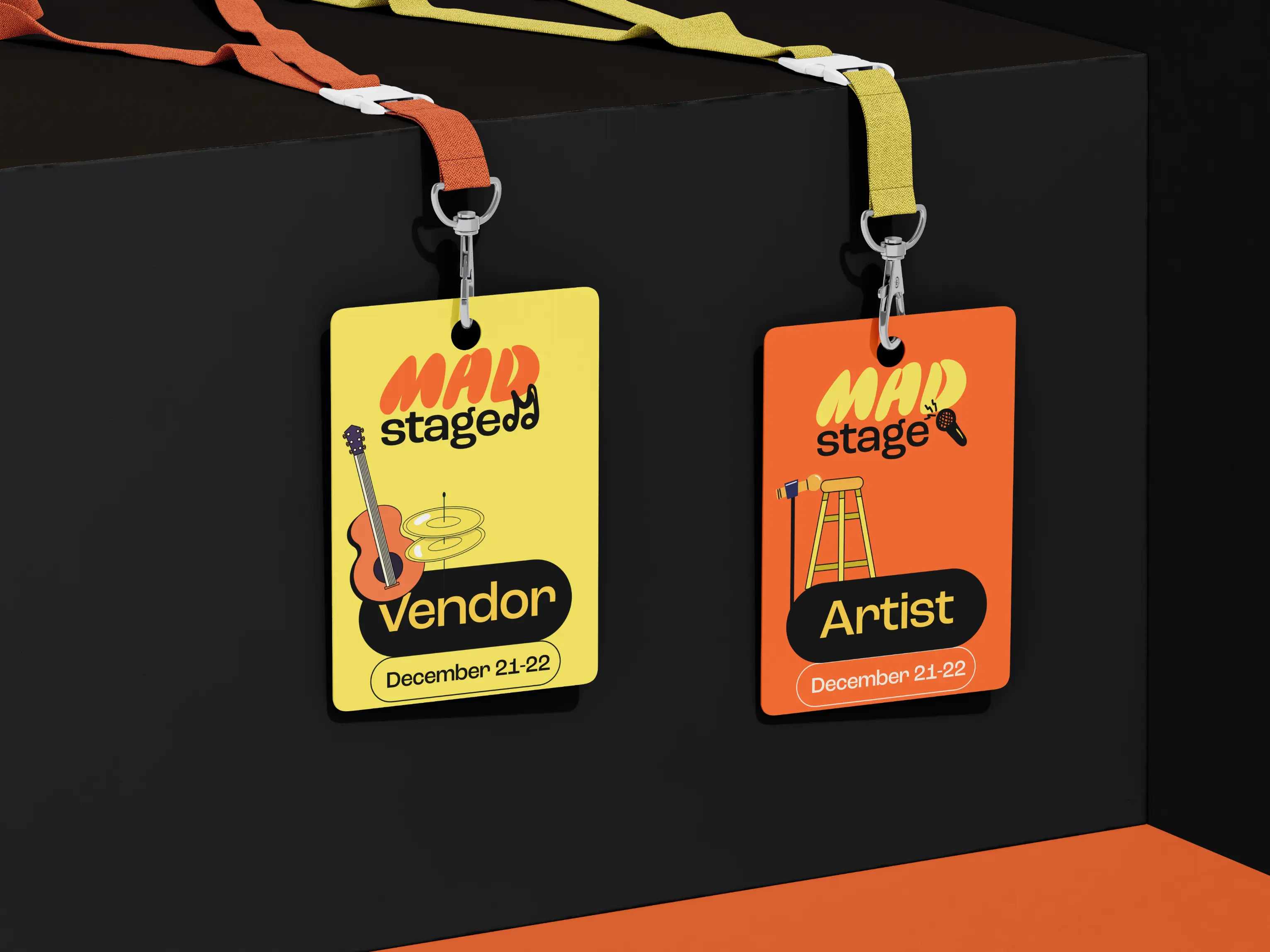 Two event badges hanging on a black wall: yellow badge labeled Vendor with guitar and cymbals design, and orange badge labeled Artist with microphone and stool design, both dated December 21-22.