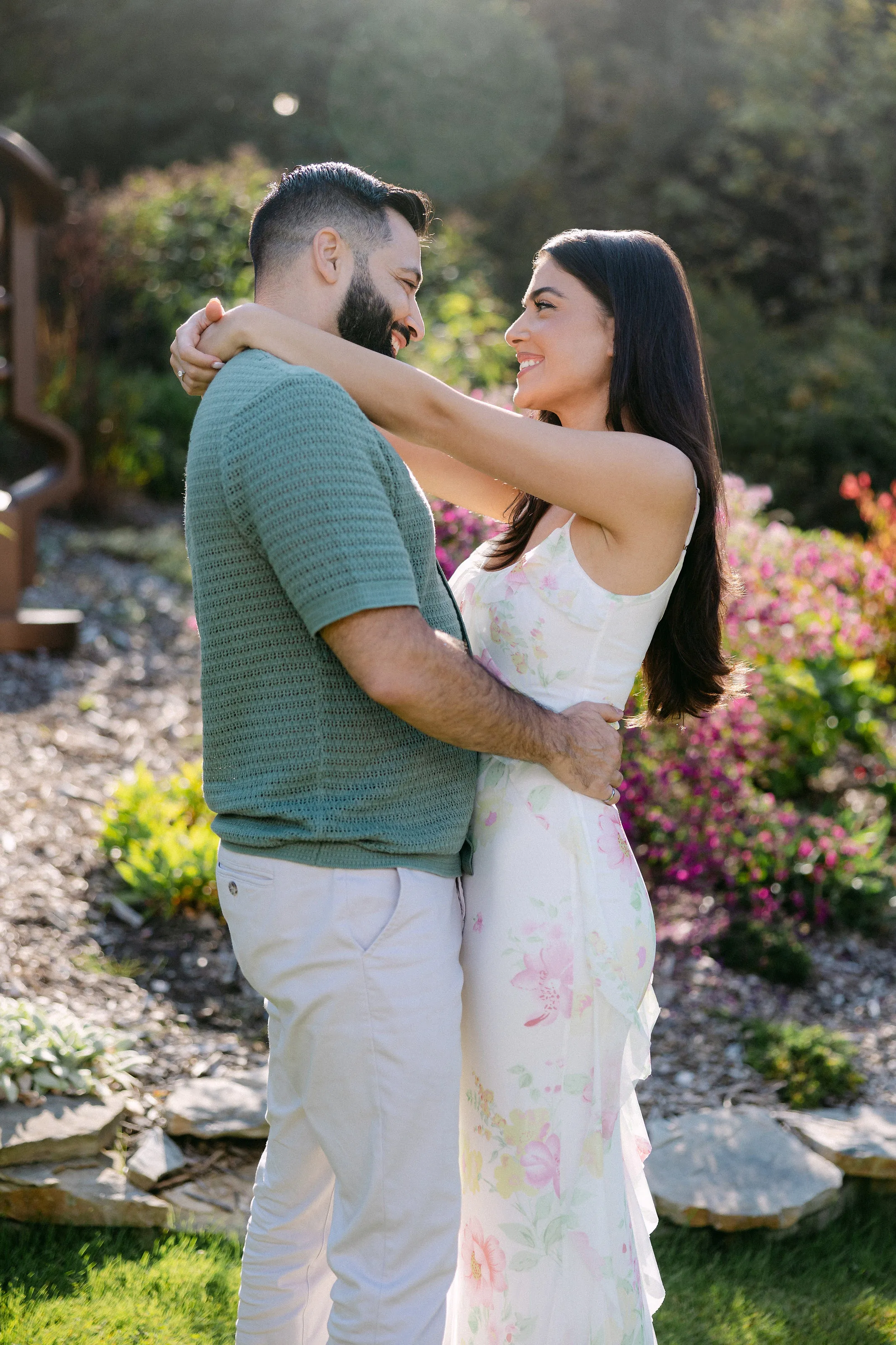 Couple de fiancés enlacés se souriant dans un jardin fleuri ensoleillé