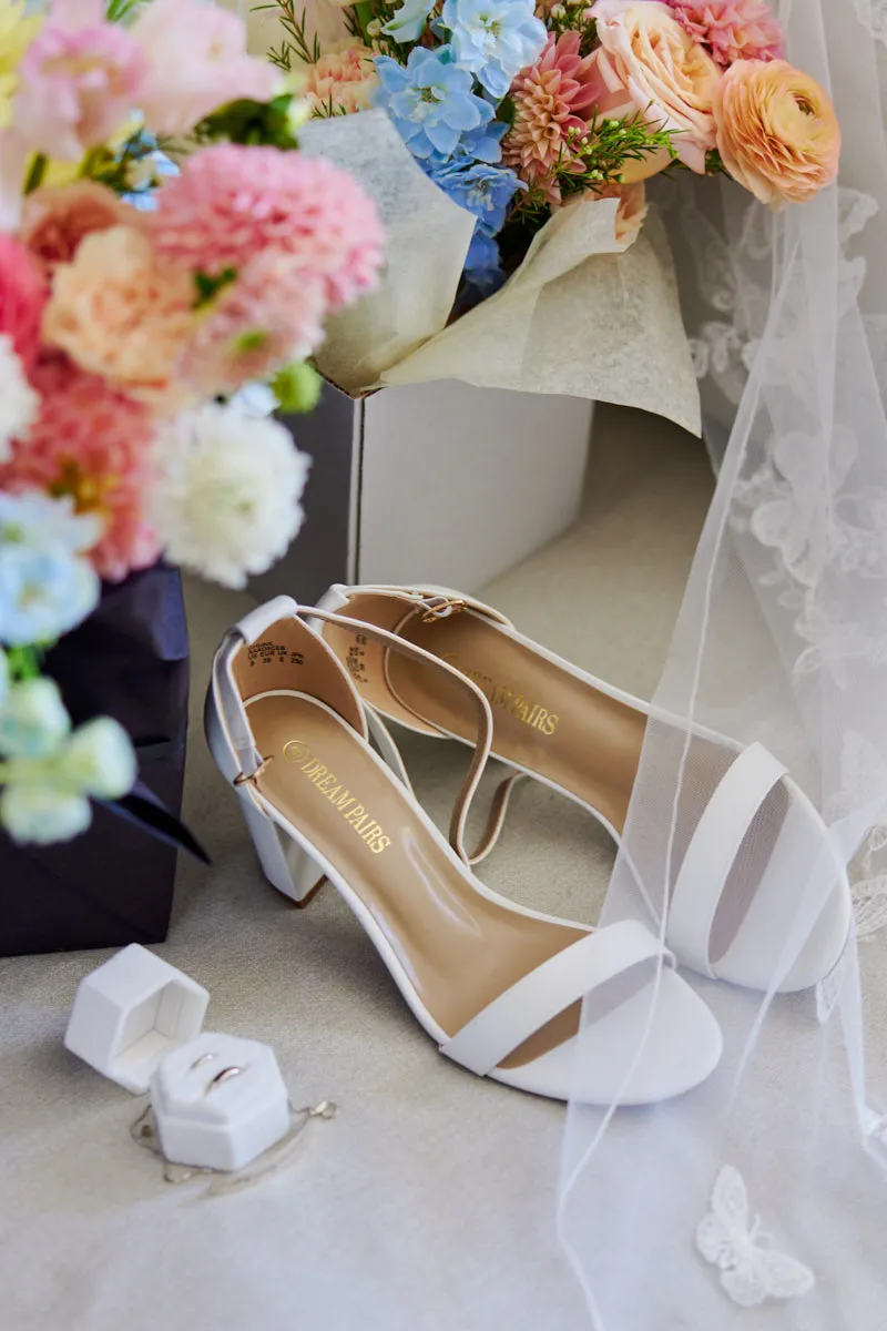 Détails de mariage de la mariée : sandales blanches à talons, écrin à bague et bouquet pastel près d'un voile de dentelle