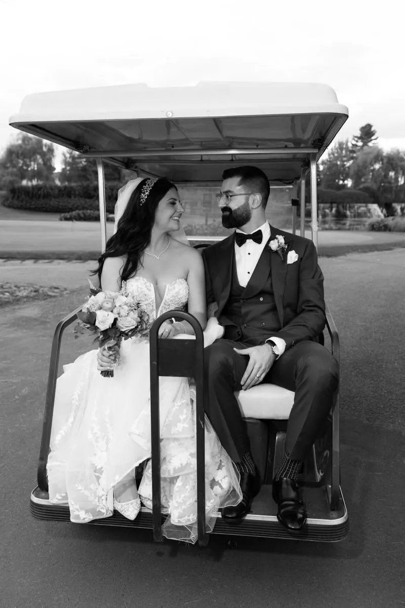Photo en noir et blanc des mariés se souriant dans une voiturette de golf