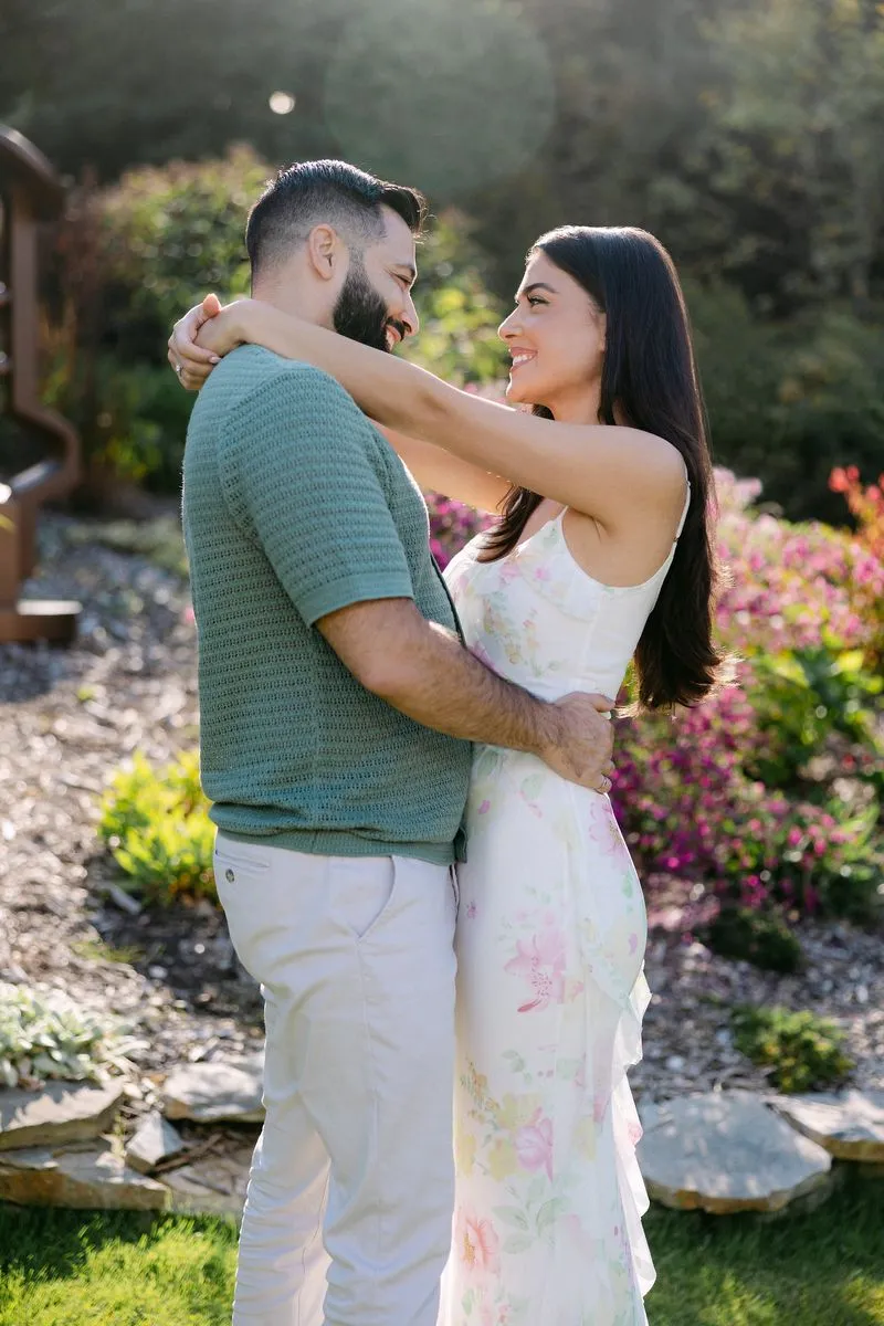 Engaged couple embracing and smiling at each other in a sunny flower garden