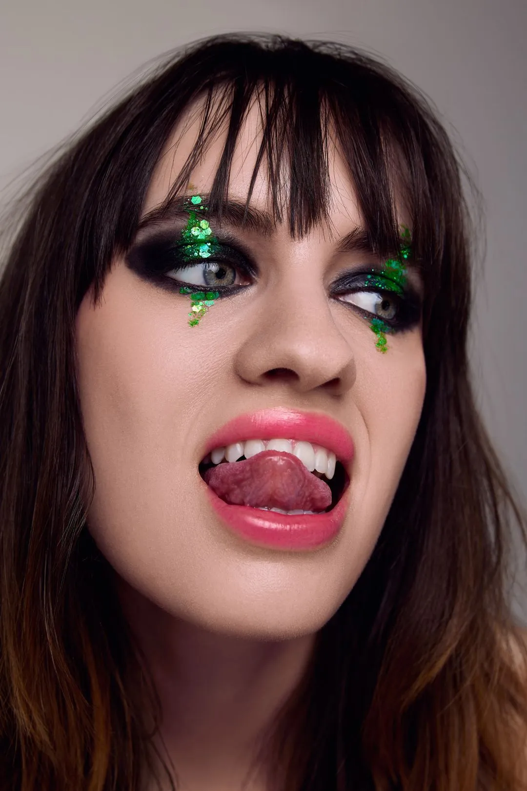 Portrait éditorial d'une mannequin aux yeux charbonneux, larmes de paillettes vertes et langue tirée