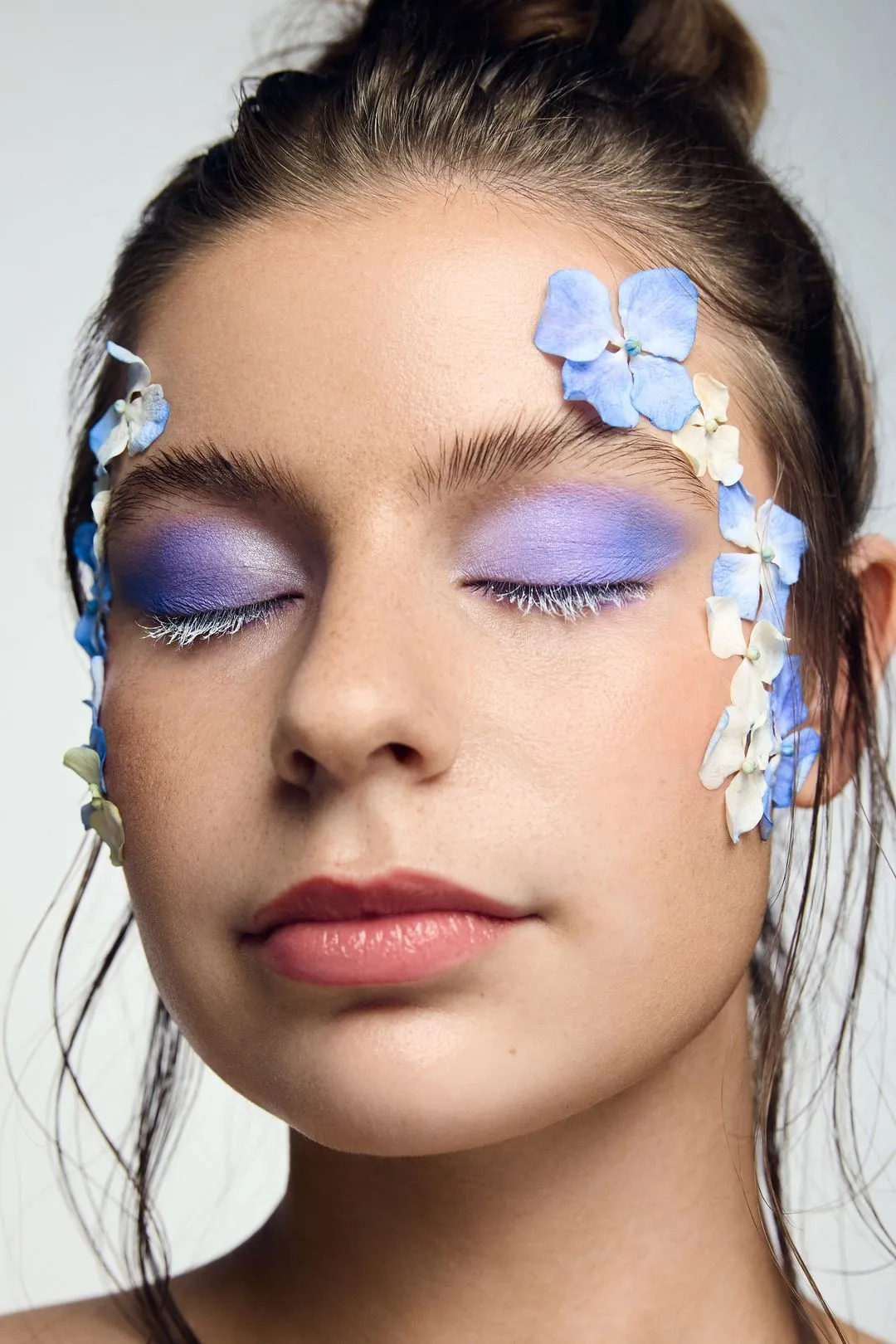 Portrait beauté d'une mannequin au fard lavande, des fleurs bleues sur le visage