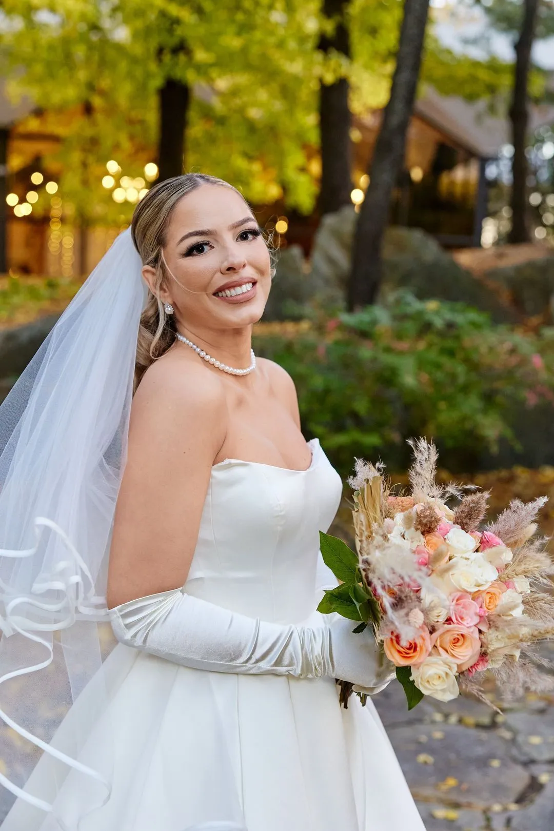 Bride in a strapless gown and long satin gloves smiling with her bouquet