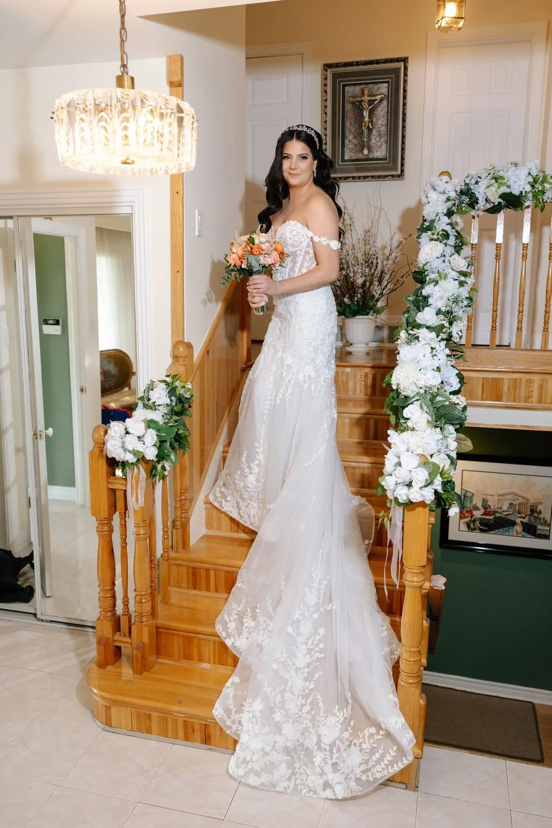 Bride in a lace gown posing on a staircase decorated with white flowers