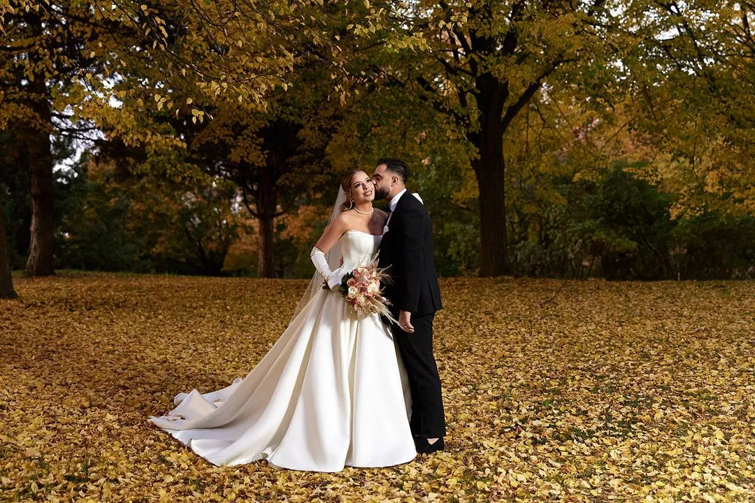 Bride and groom sharing a moment in a park covered in golden autumn leaves