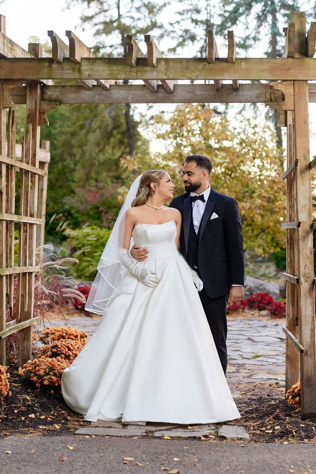 Bride and groom standing under a wooden pergola in a garden in autumn