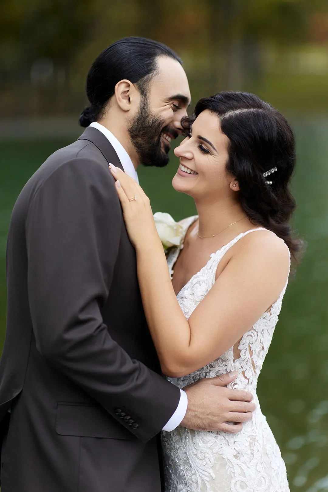 Bride and groom embracing and smiling cheek to cheek outdoors