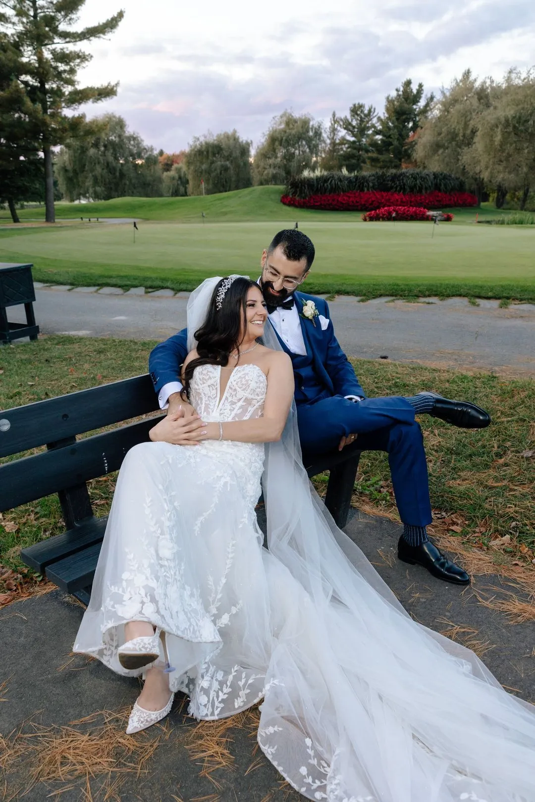 Bride and groom sitting together on a bench overlooking a golf course