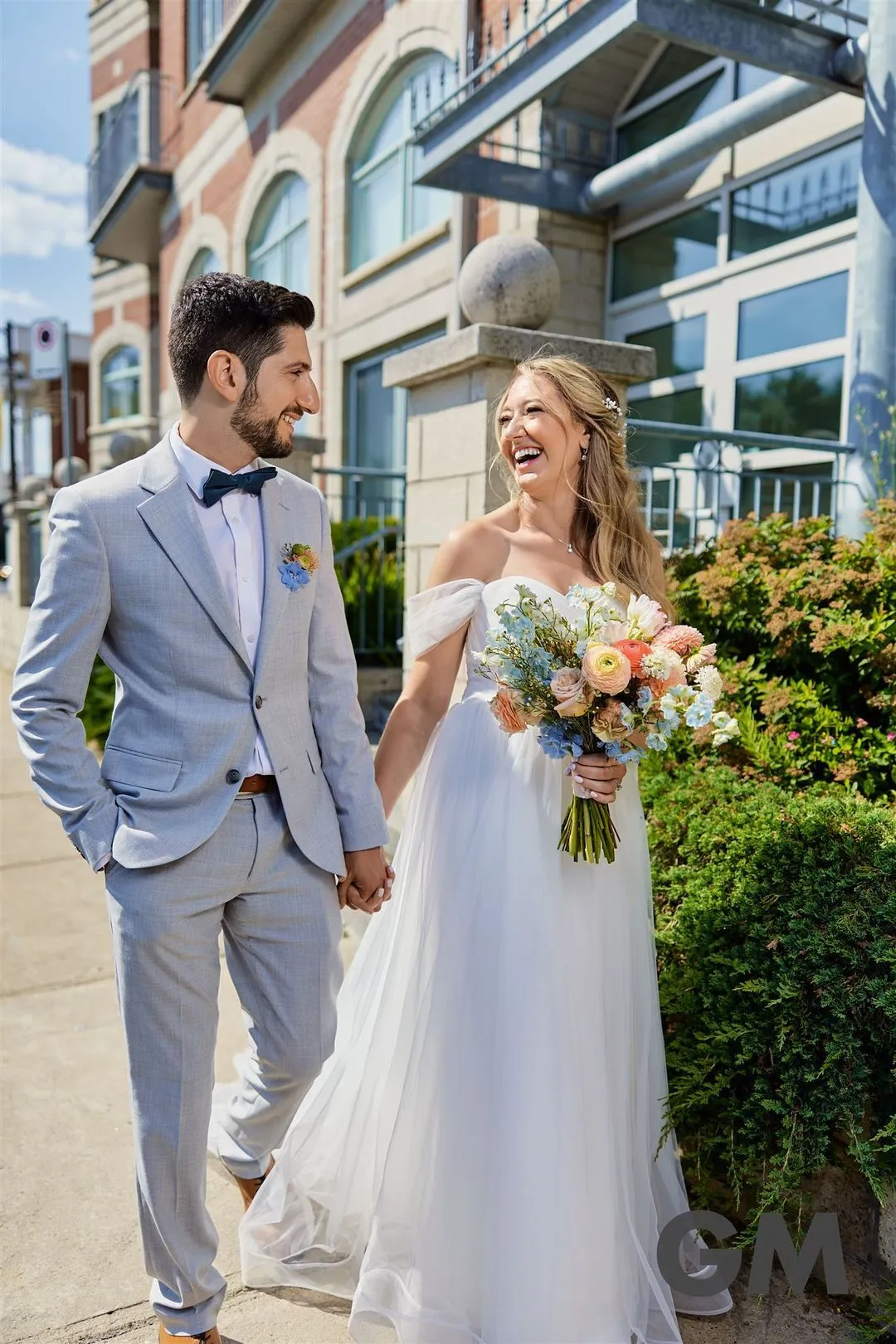 Laughing bride and groom walking hand in hand on a city sidewalk