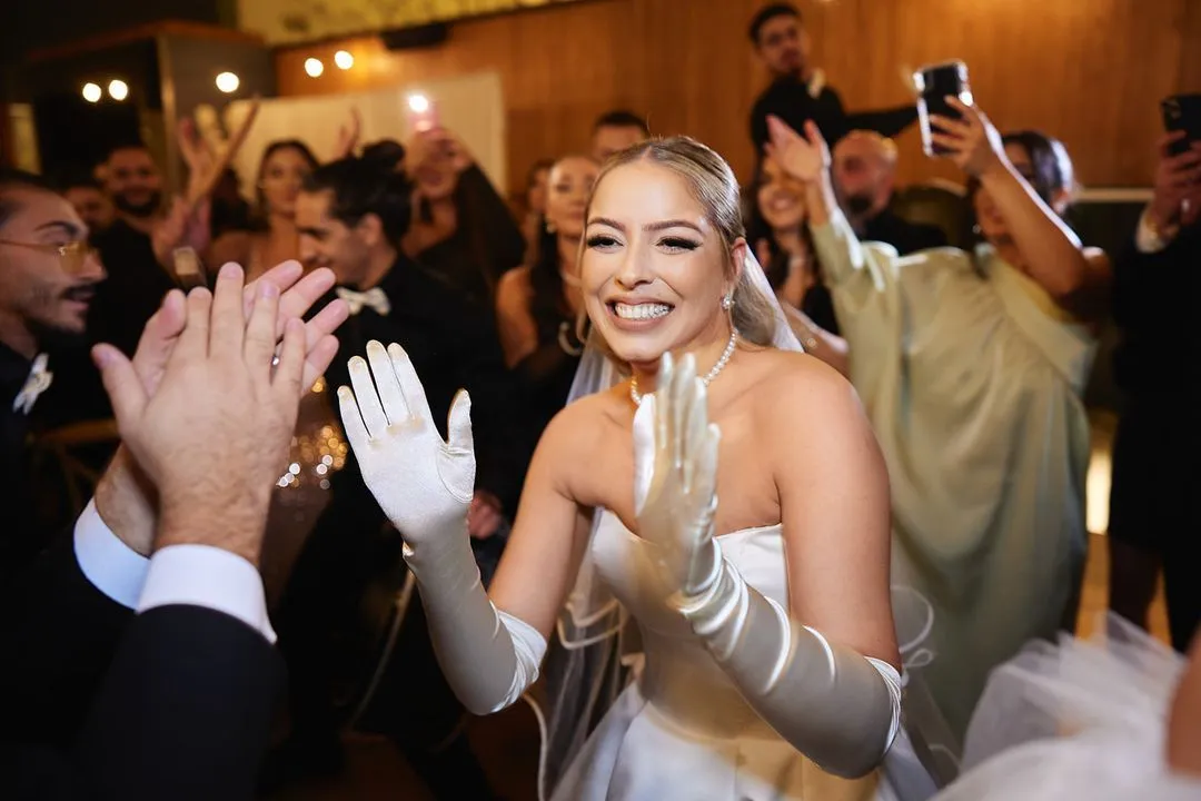 Bride in long satin gloves clapping and smiling with guests at the wedding reception