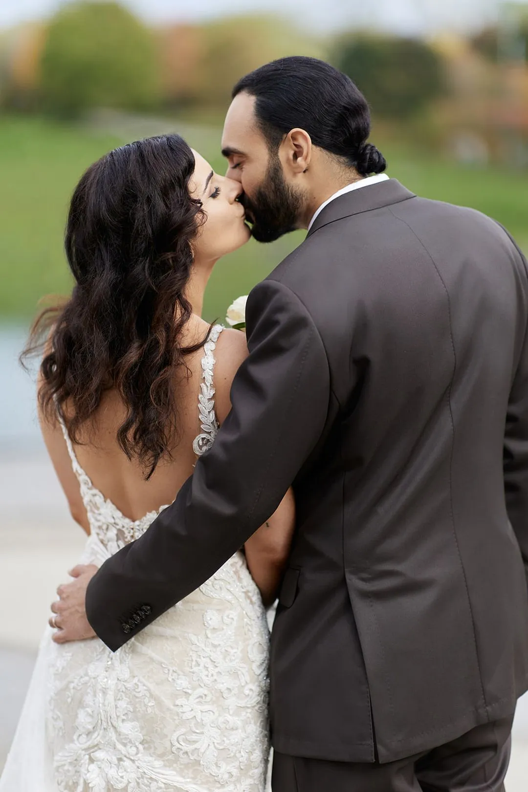 Groom kissing the bride outdoors, her open-back lace gown in view