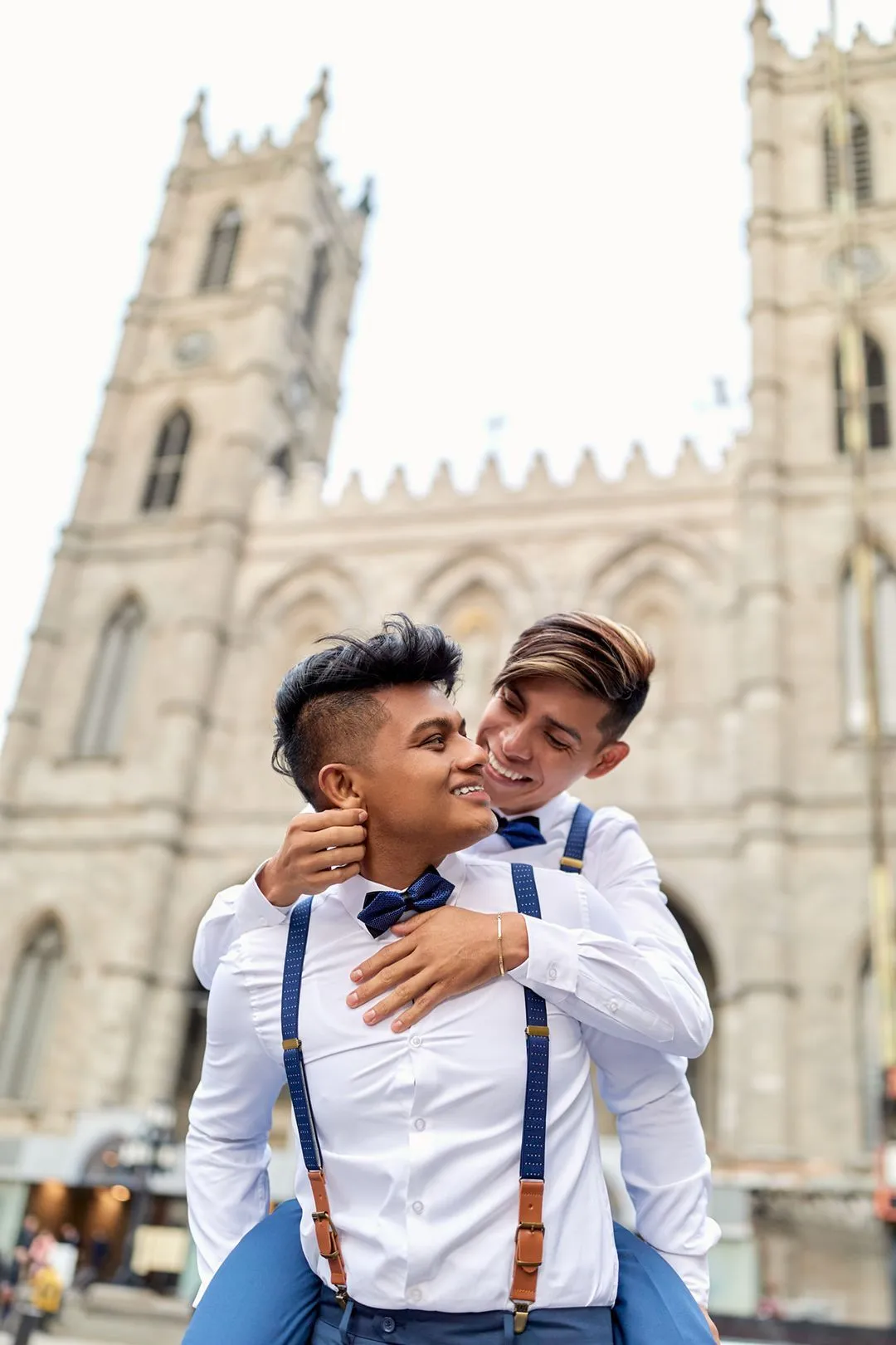 Deux hommes en nœud papillon et bretelles, enlacés devant la basilique Notre-Dame de Montréal