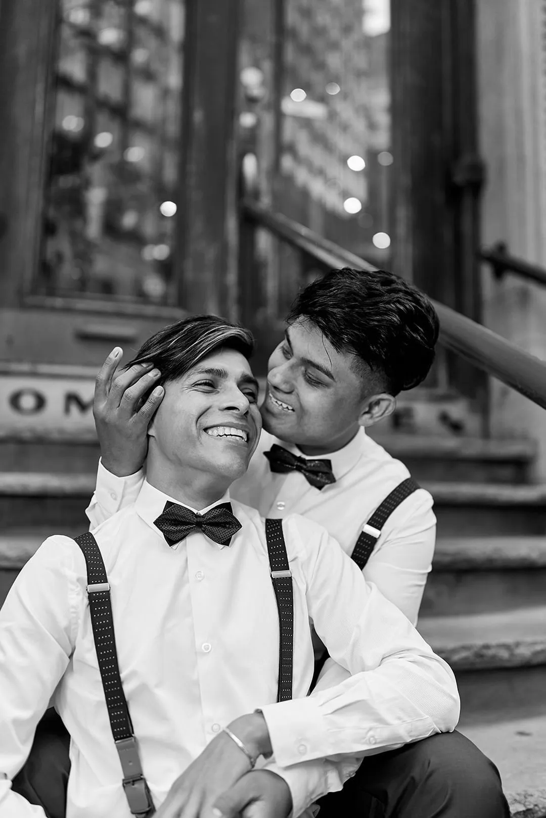 Photo en noir et blanc de deux hommes en nœud papillon partageant une étreinte joyeuse sur des marches de pierre