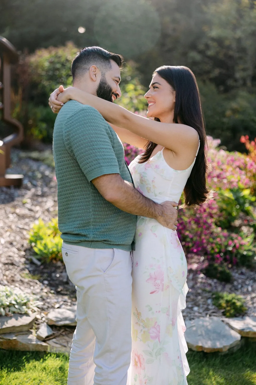 Couple de fiancés enlacés se souriant dans un jardin fleuri ensoleillé