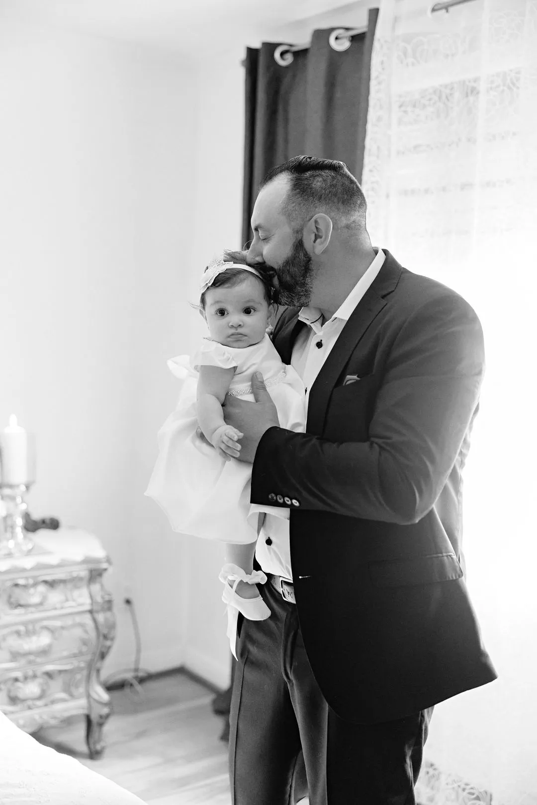 Photo en noir et blanc d'un homme tenant et embrassant un bébé en robe de baptême