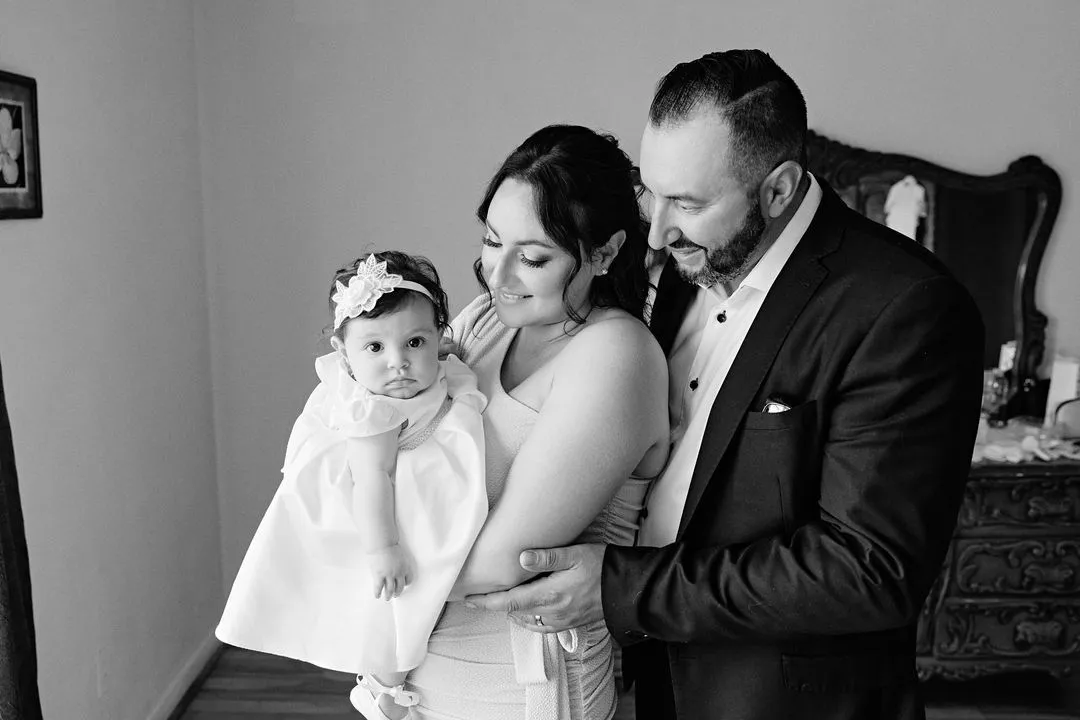 Photo en noir et blanc d'un couple tenant son bébé en robe de baptême
